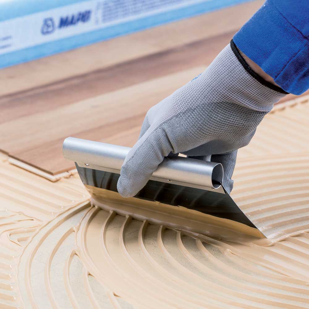 Person using a mapei trowel on wooden flooring installation