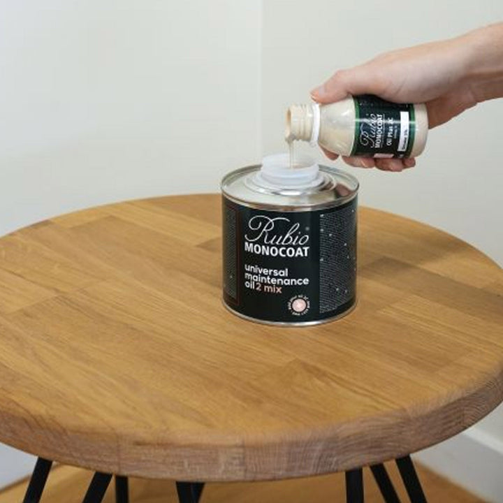 Person pouring a liquid into a can of Rubio Monocoat on a wooden table.